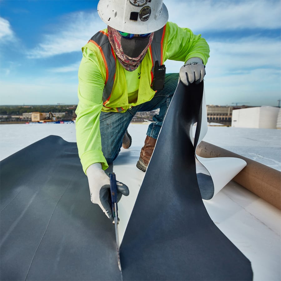 Roofer in safety gear atop the Savannah Convention Center cutting sheet of PVC membrane.