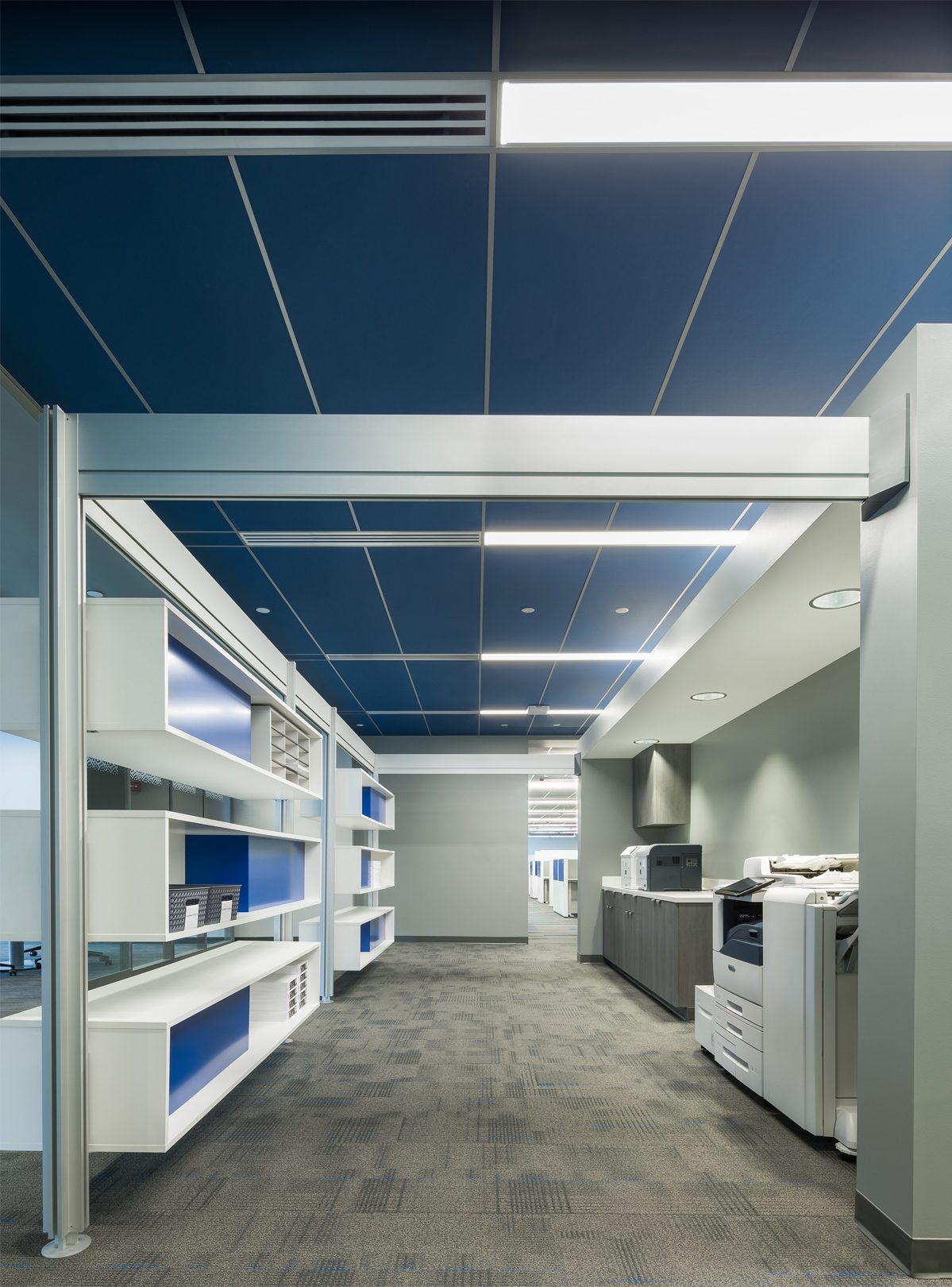 Organized office printing area with blue ceiling tile system.