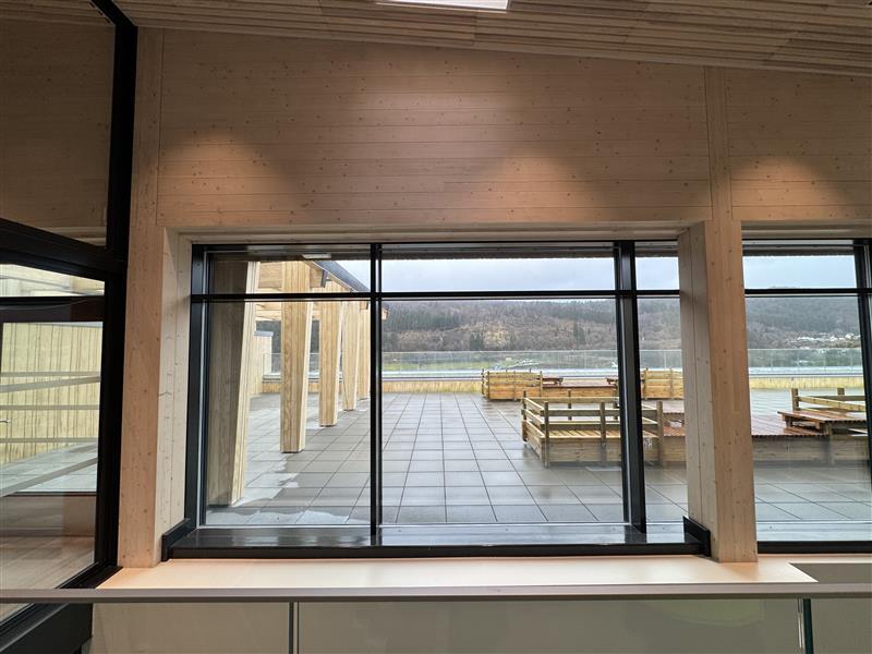 Modern wooden interior with large windows viewing a patio, lake, and wooded hills.