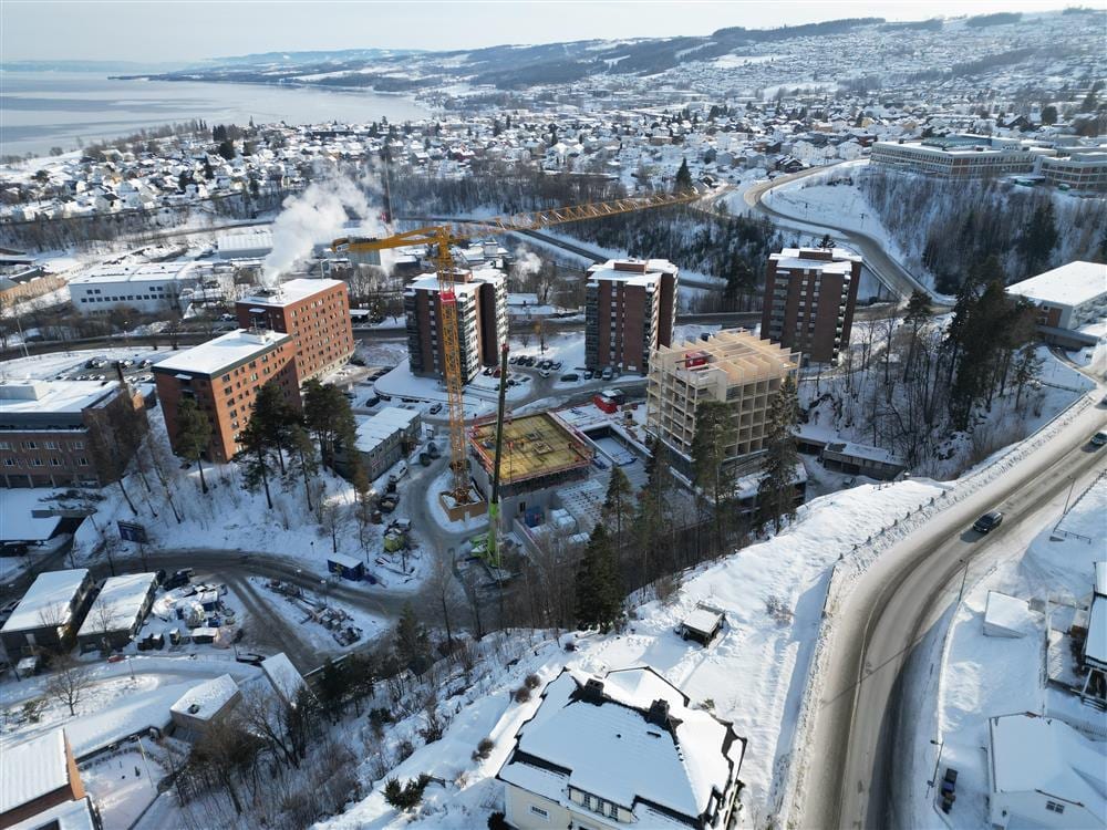Snowy aerial view of a town with construction, cranes, and a lake.