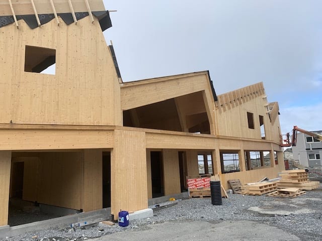 Modern wooden building under construction with gabled roofs and multiple levels.