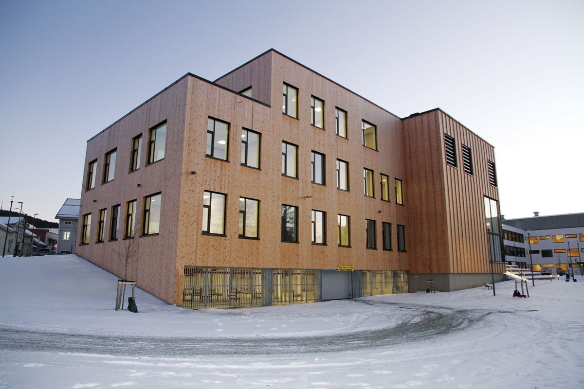 Modern building with light wood siding and many windows, surrounded by snow under a clear sky.