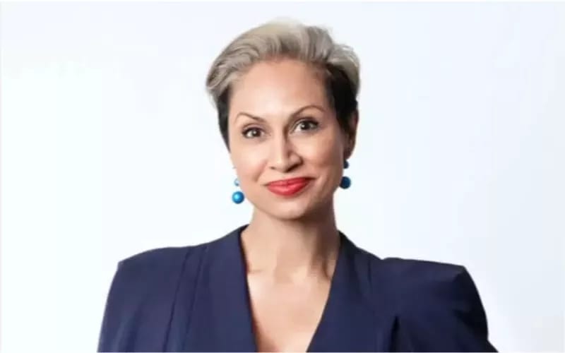Headshot of a smiling woman with short, two-toned hair, red lipstick, and blue earrings, wearing a navy blazer.