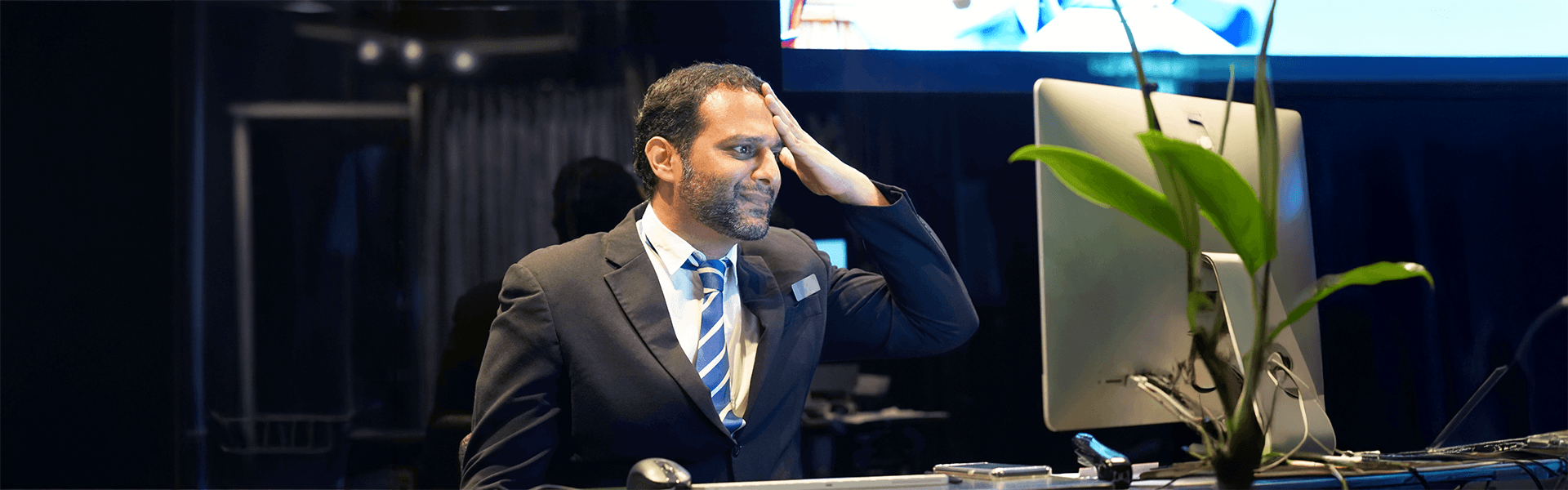 Man in suit and tie with hand on forehead, beside a computer.