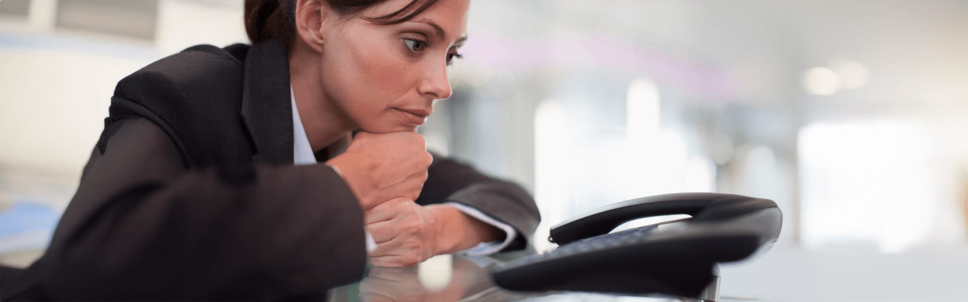 Pensive businesswoman in a suit looking at a desk telephone.