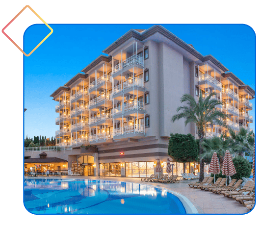 Illuminated hotel building with balconies, a swimming pool, and palm trees at dusk.