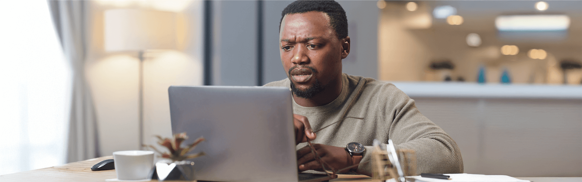 Black man with furrowed brow looking intently at laptop on desk.
