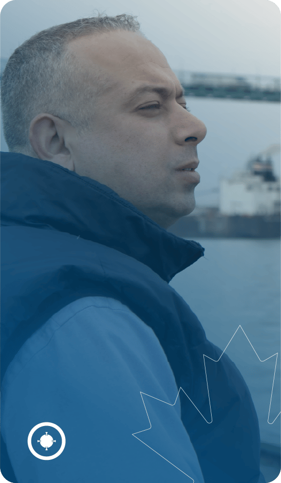 Person looking into the distance with blue coat and ship and river in the background.
