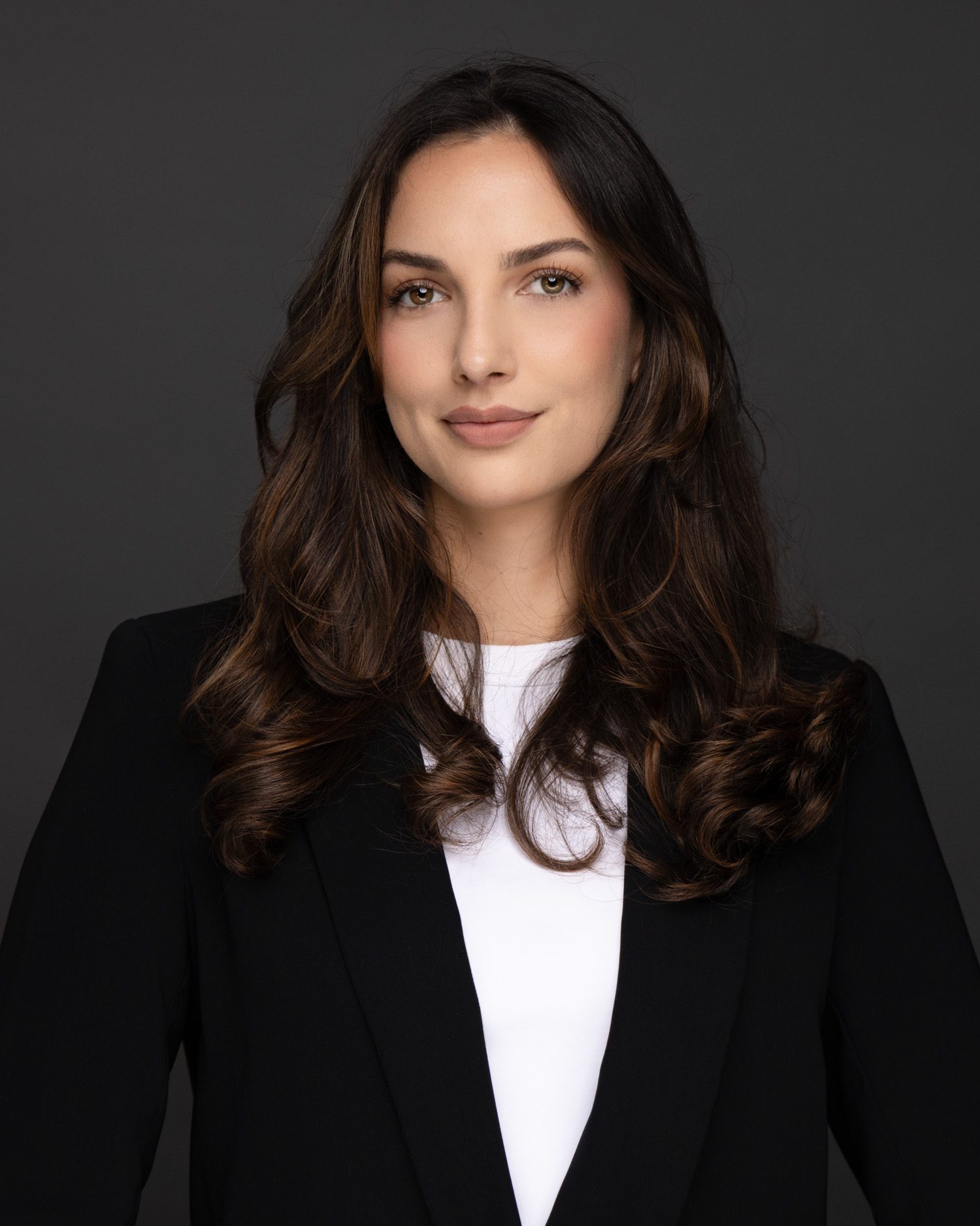 Professional headshot of a woman with dark wavy hair, black blazer, and white shirt.