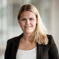 Blonde woman in black blazer and white top, smiling at the camera.