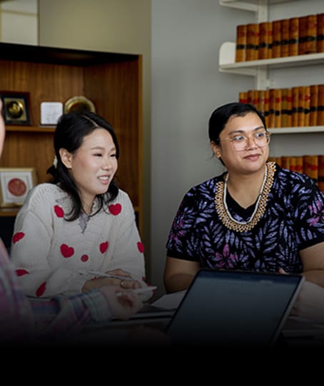 Two diverse women in a meeting, one smiling, in an office with bookshelves.