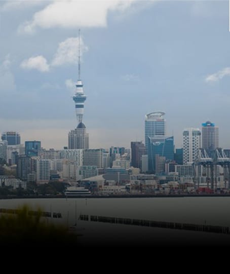 Auckland city skyline with Sky Tower and harbor under a cloudy sky.