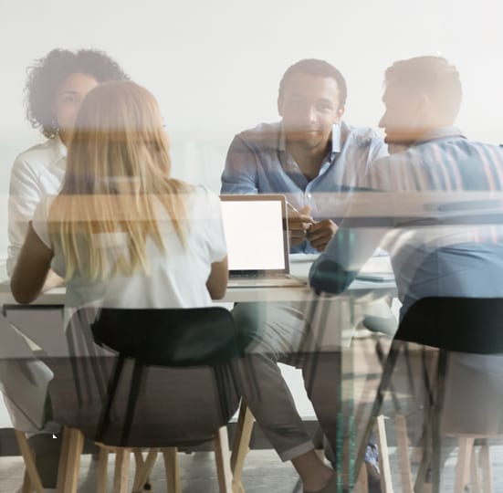 A diverse group of colleagues collaborating around a table with a laptop in a brightly lit office setting.