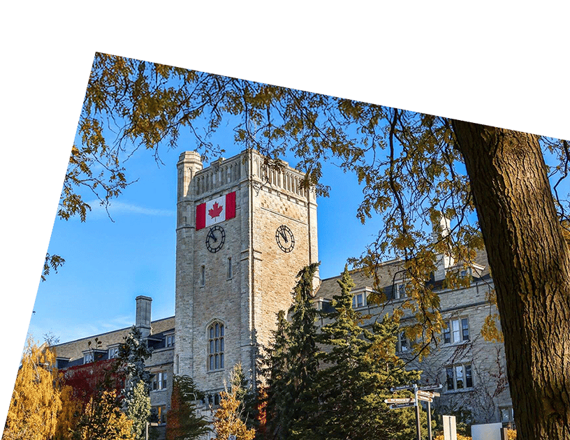 Canadian flag on a stone university clock tower, autumn trees, and blue sky.