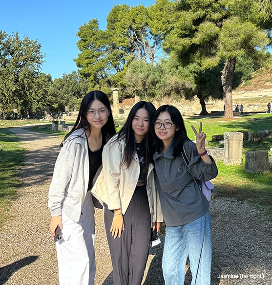 Three smiling Asian women pose at an ancient ruin site, one making a peace sign.
