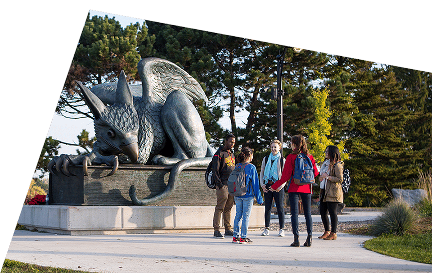 A bronze griffin statue with a group of students on a college campus.