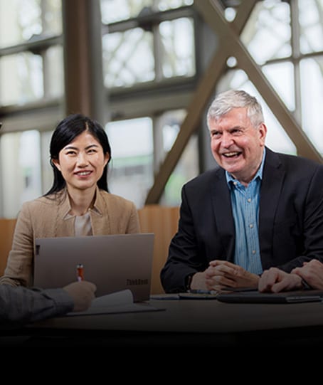 Smiling Asian woman & laughing older man at meeting table with laptop.