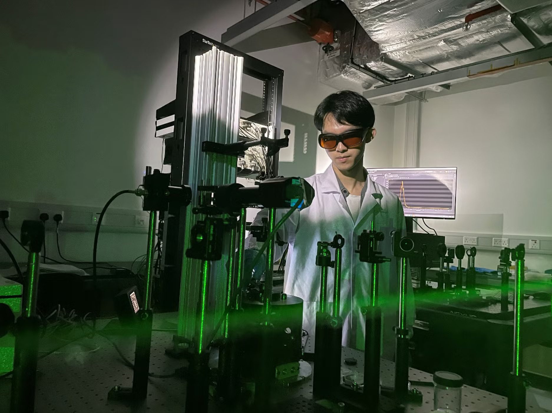 Researcher in lab coat and goggles working with a laser experiment.