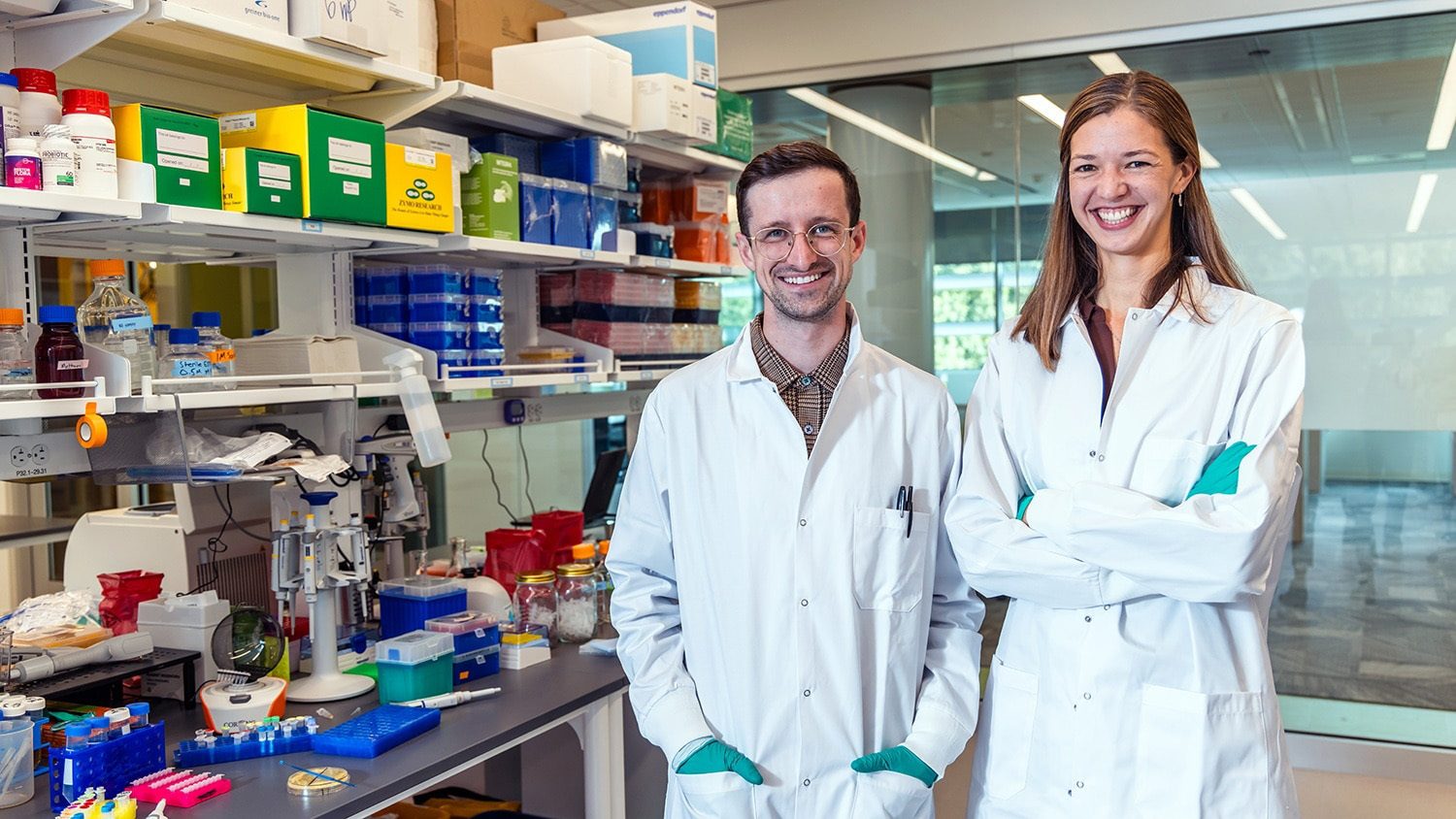 Two smiling scientists in lab coats in a lab.