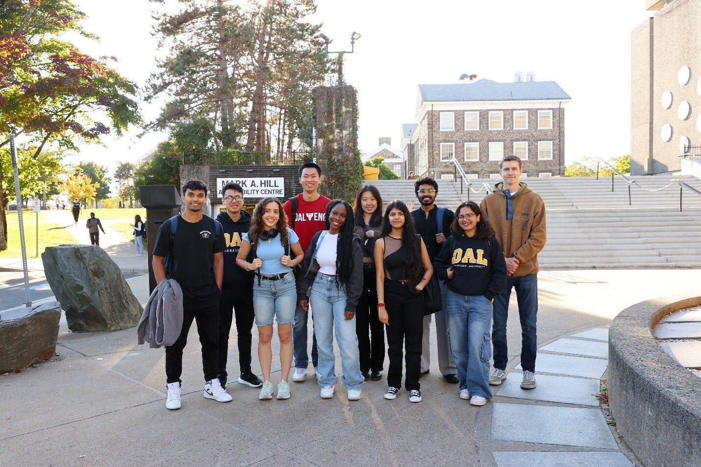 A diverse group of students smiles for a photo outside on a college campus.