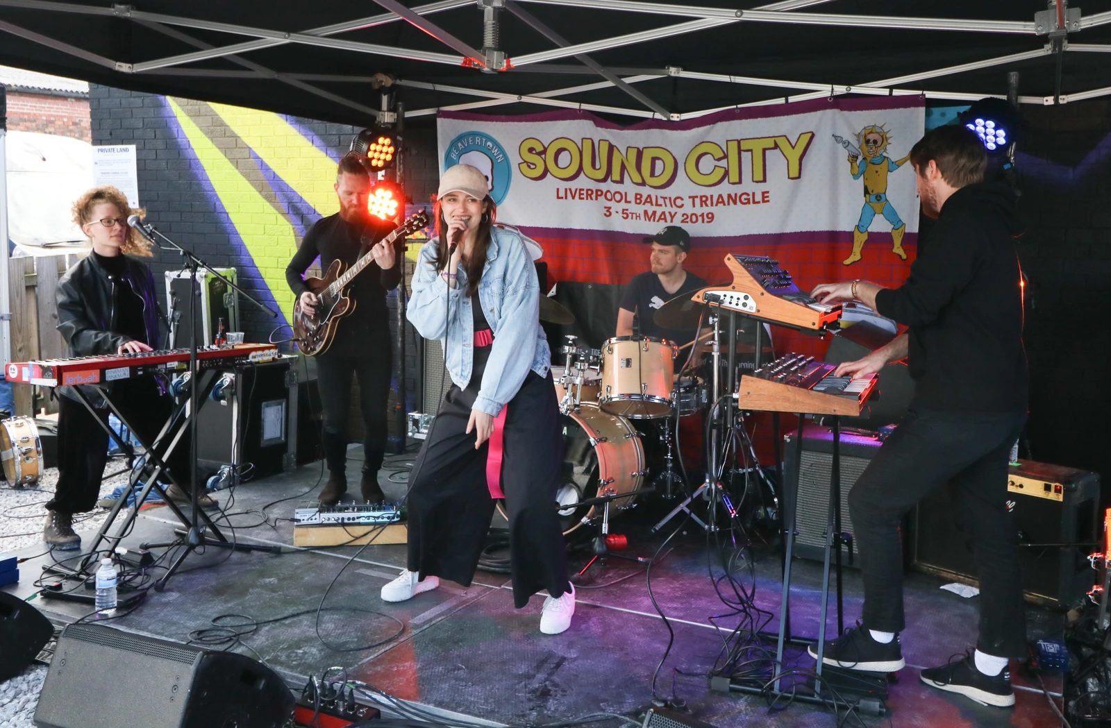 A band performs live on an outdoor stage under a "Sound City" festival banner.