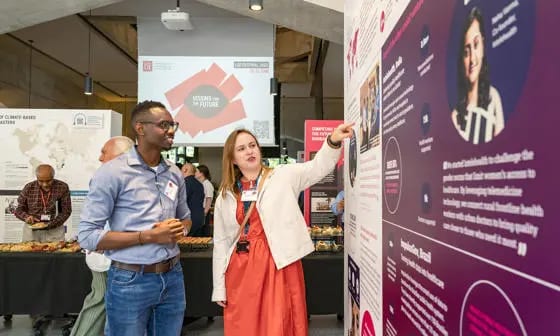 A man and woman at a conference, the woman pointing at an informational display.