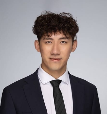 Headshot of a young Asian man in a suit and tie, with curly hair.