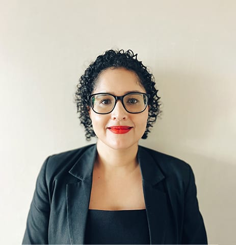 Smiling woman with curly hair, glasses, red lipstick, and black blazer.