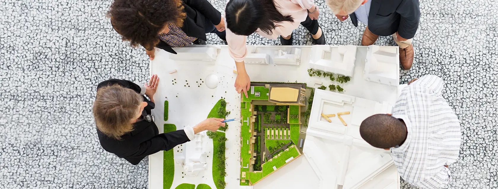 Overhead view of people gathered around an architectural model with green spaces and buildings.