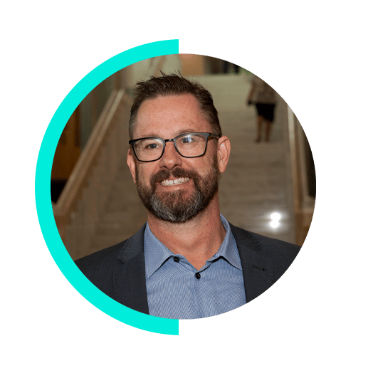 Smiling man with glasses and beard, wearing a suit jacket, in a circular frame.