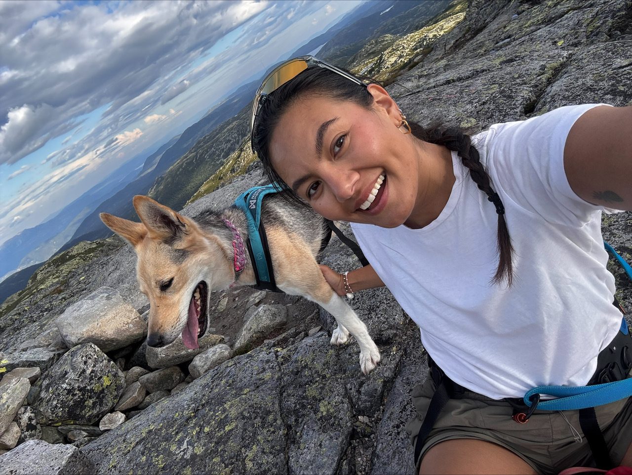 Smiling woman and panting dog in a mountain selfie with a vast landscape behind.
