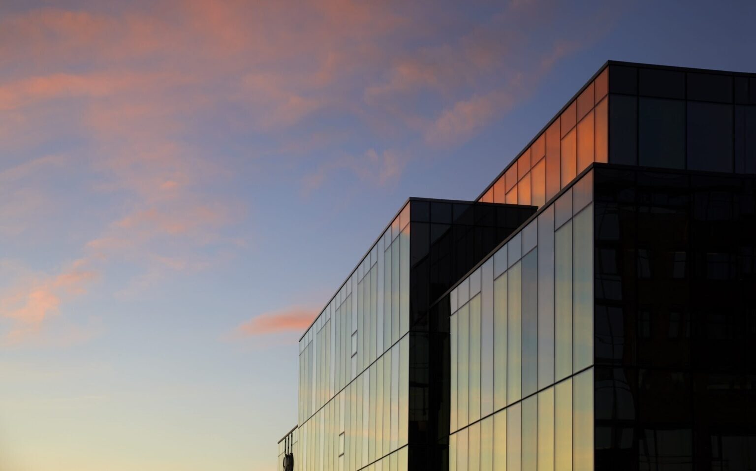 Glass building with pink-orange sunset reflections and blue sky.