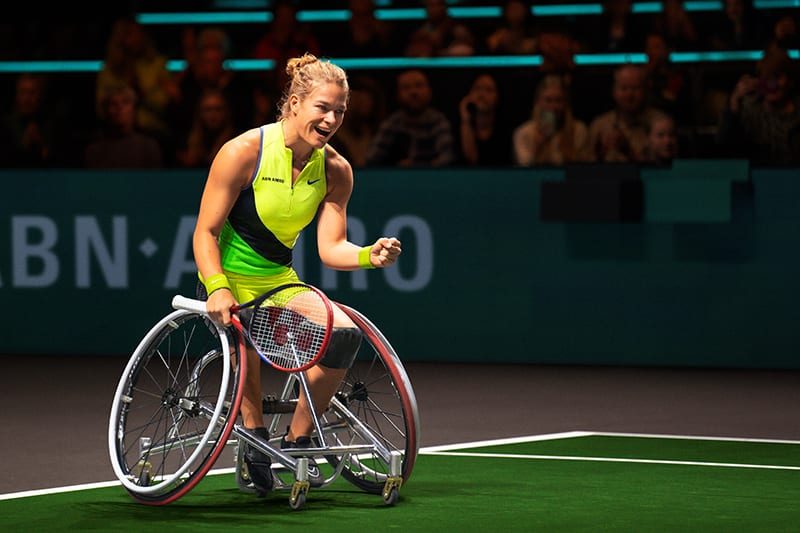 Smiling wheelchair tennis player celebrating on court, holding a racket.