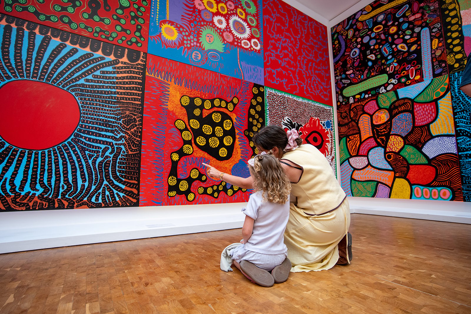 Woman and child viewing vibrant, patterned abstract art in a gallery, pointing at a detail.