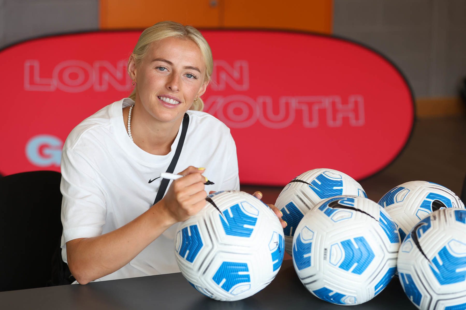 Chloe Kelly signing a football whilst smiling