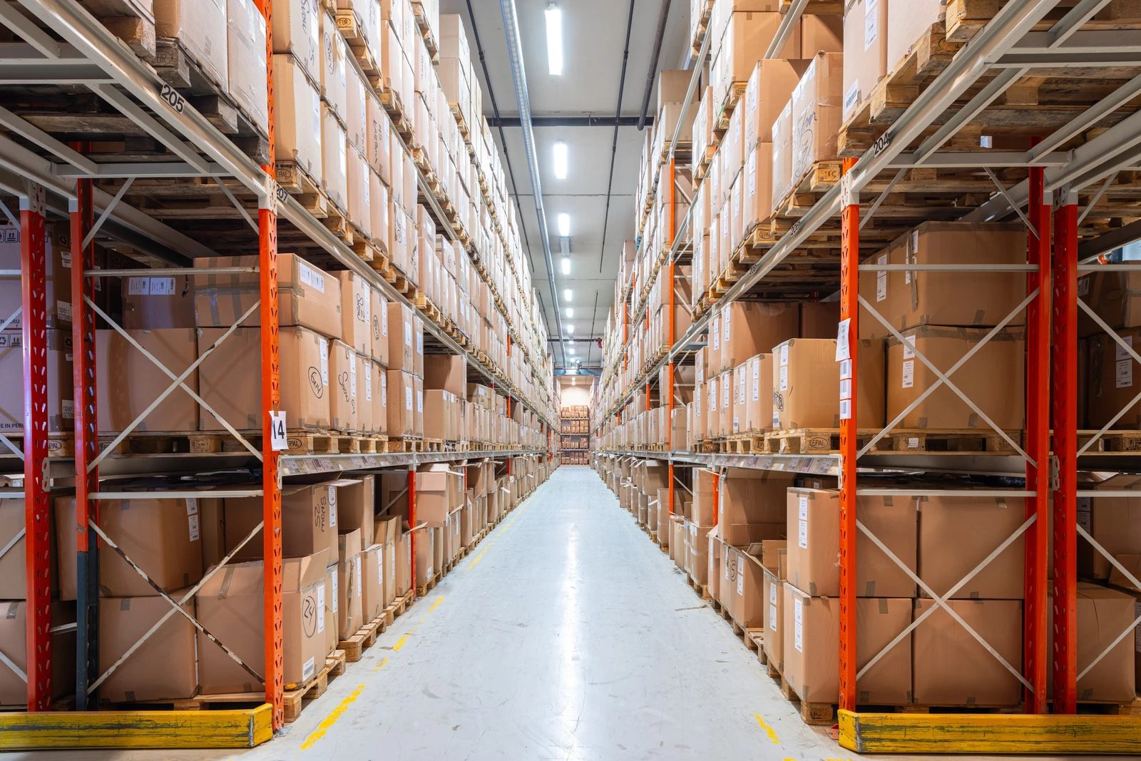 Long warehouse aisle filled with shelves of stacked cardboard boxes.