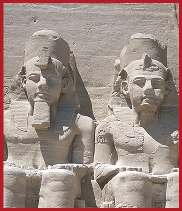 Two colossal ancient Egyptian pharaoh statues carved in rock, featuring elaborate headdresses.
