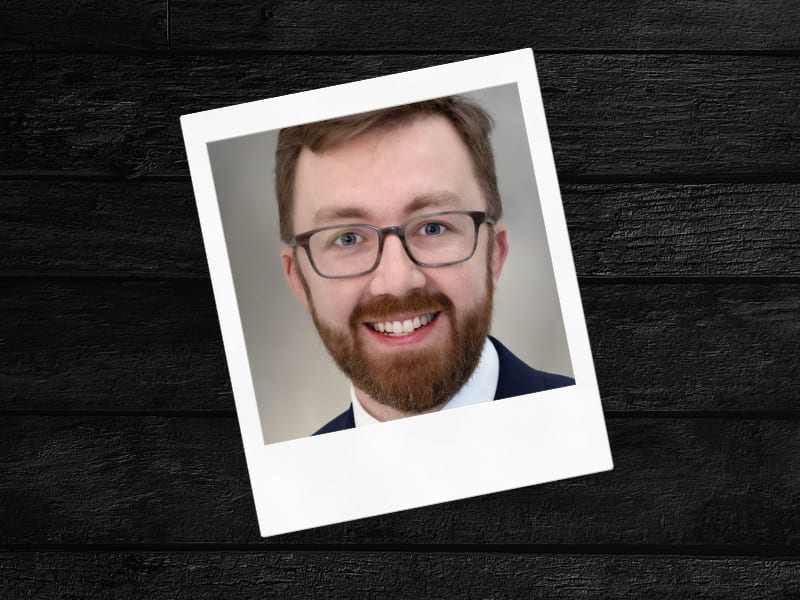 A smiling man with glasses and a beard in a polaroid photo.
