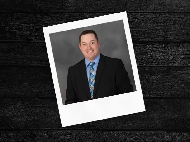 Smiling man in a suit in a tilted Polaroid frame on a dark wooden background.