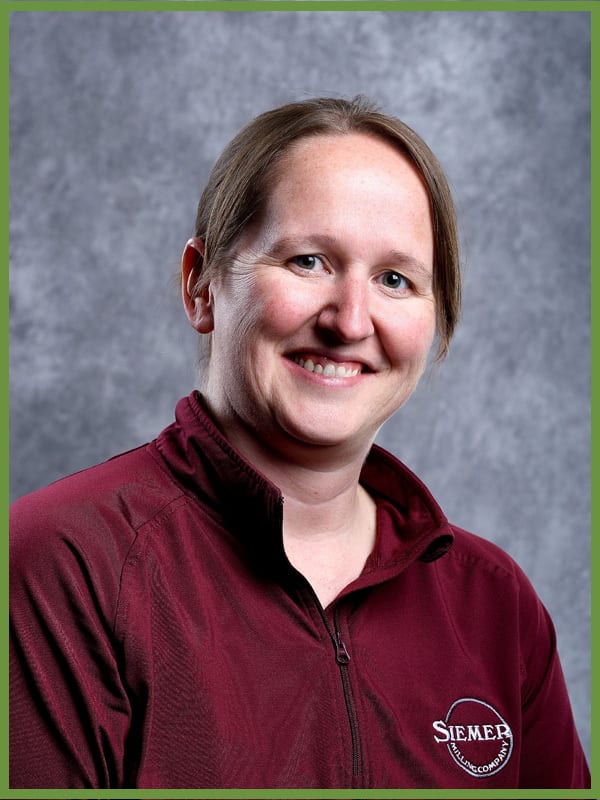 Smiling woman in maroon jacket with "SIEMER" logo.