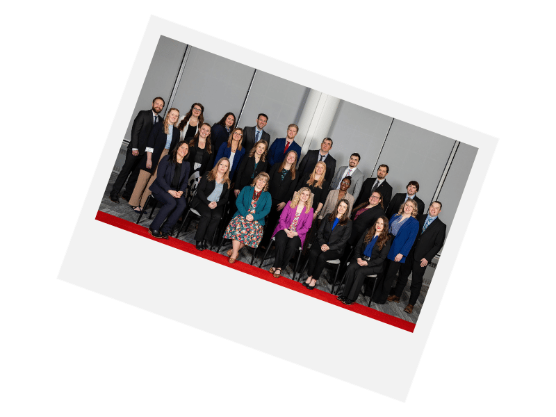 Group portrait of business professionals, standing and sitting on a red carpet.