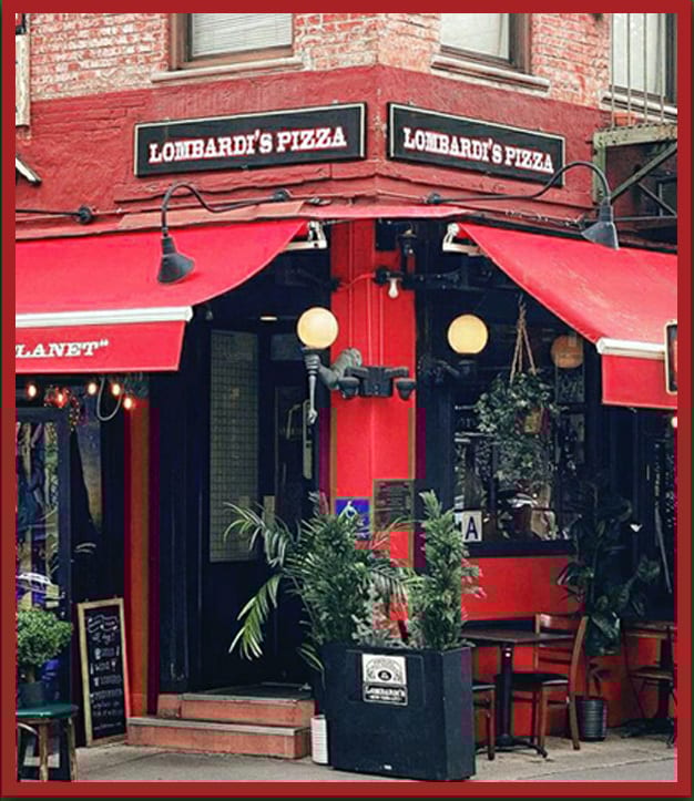 Corner view of Lombardi's Pizza, a red building with black trim, red awnings, and plants.