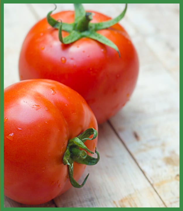 Two red tomatoes with green stems and water drops on wood.