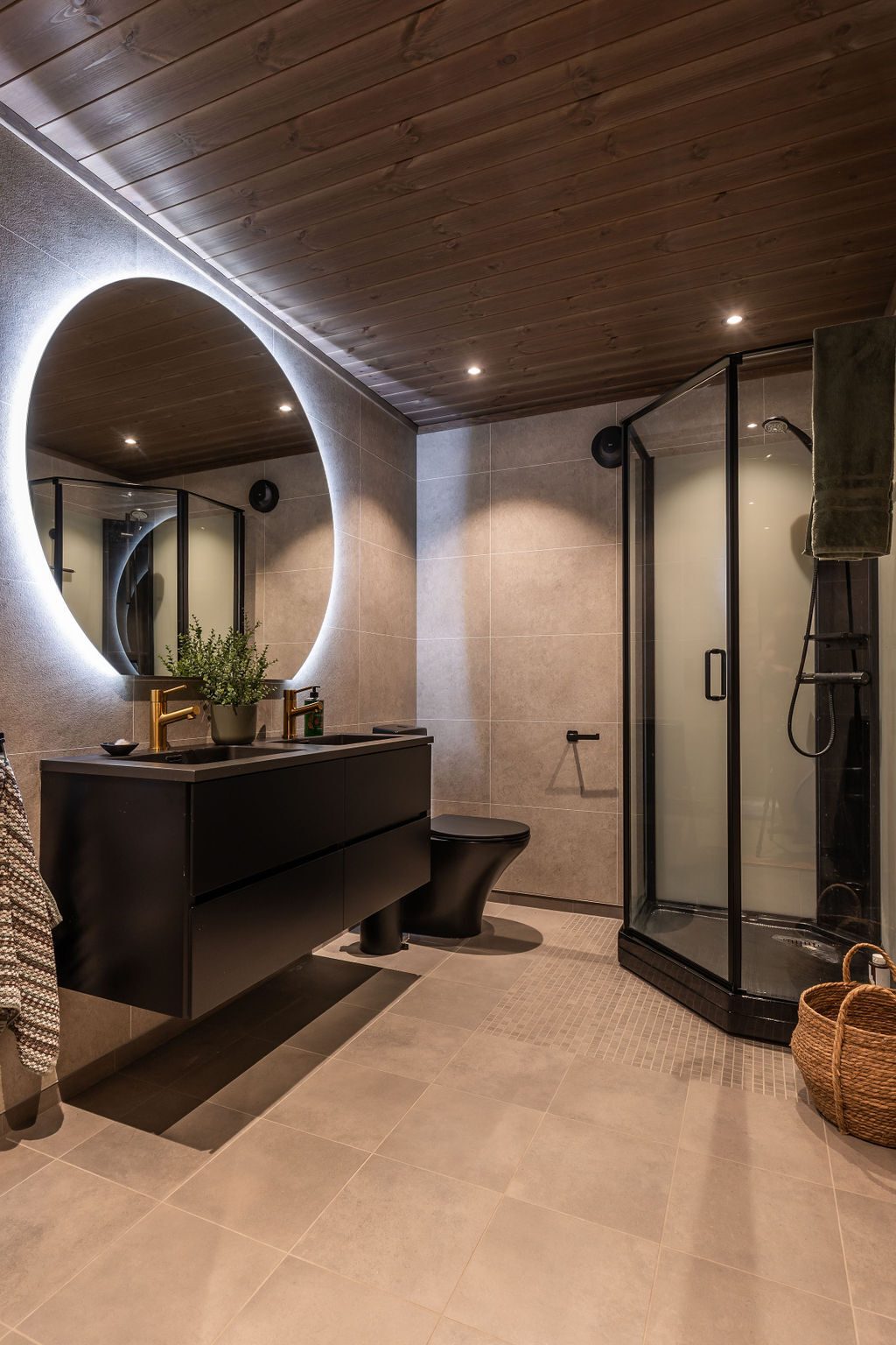 Modern bathroom with gray tiles, dark wood ceiling, black vanity, round mirror, and corner shower.