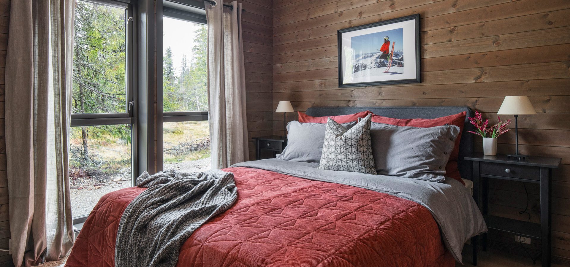 Wood-paneled bedroom with a red bed, large window overlooking a forest.