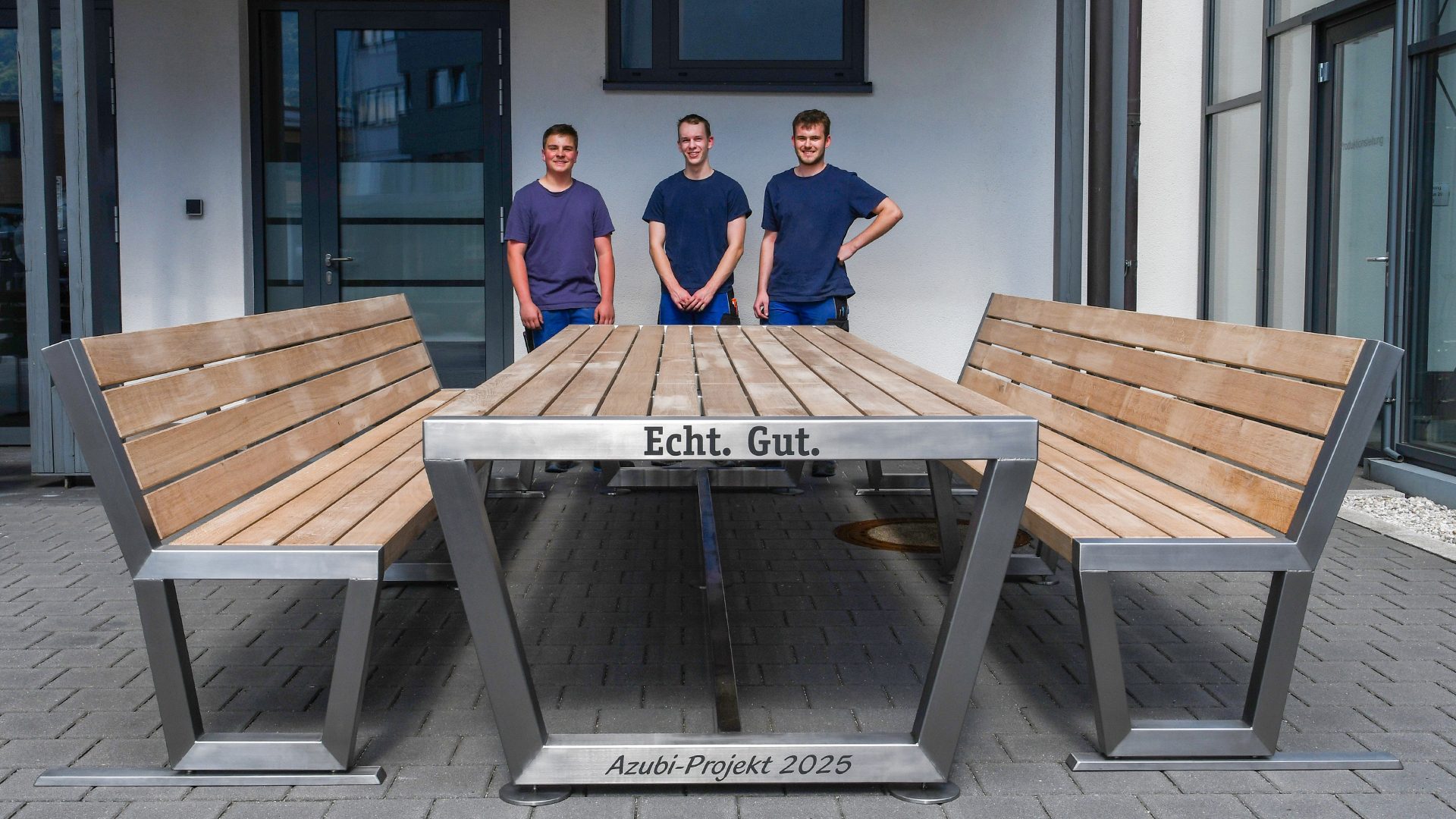 Three young men behind a custom table and benches, inscribed "Echt. Gut." and "Azubi-Projekt 2025".