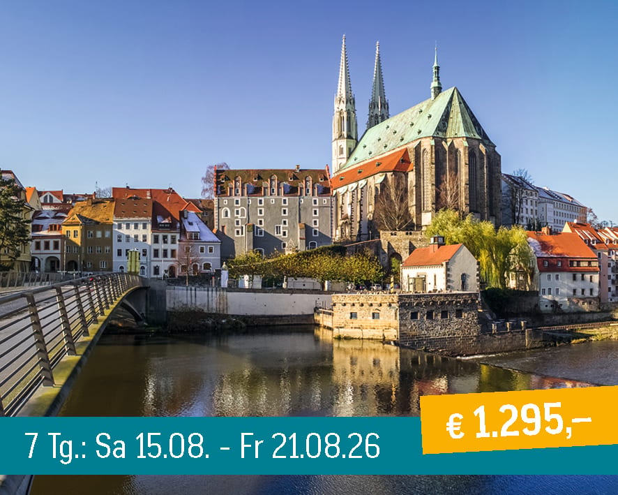 Cityscape with a river, bridge, historic buildings, and a large church under a blue sky.