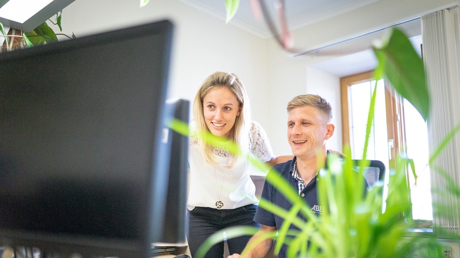 Two smiling colleagues look at a computer screen.