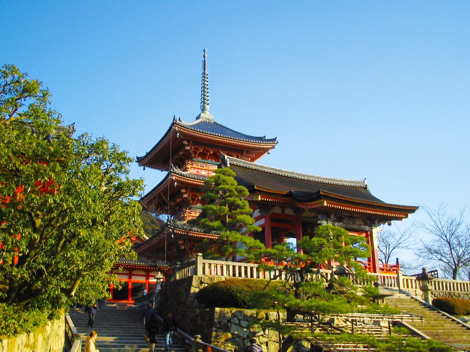A clear day view of Kiyomizu-dera Temple's pagoda and main hall, with stone stairs and lush trees.
