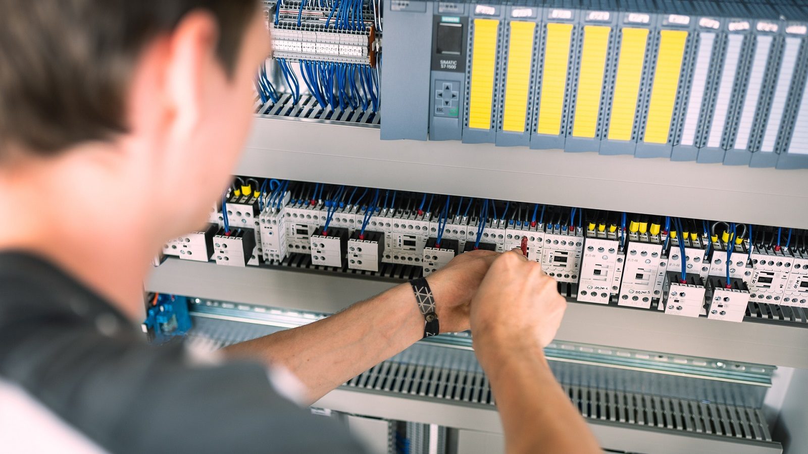 Hands connecting wires on a Siemens PLC and industrial control panel.